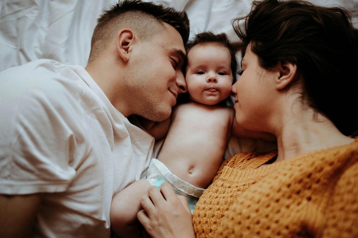 Two parents lying with their baby between them, the outcome of a donor egg cycle