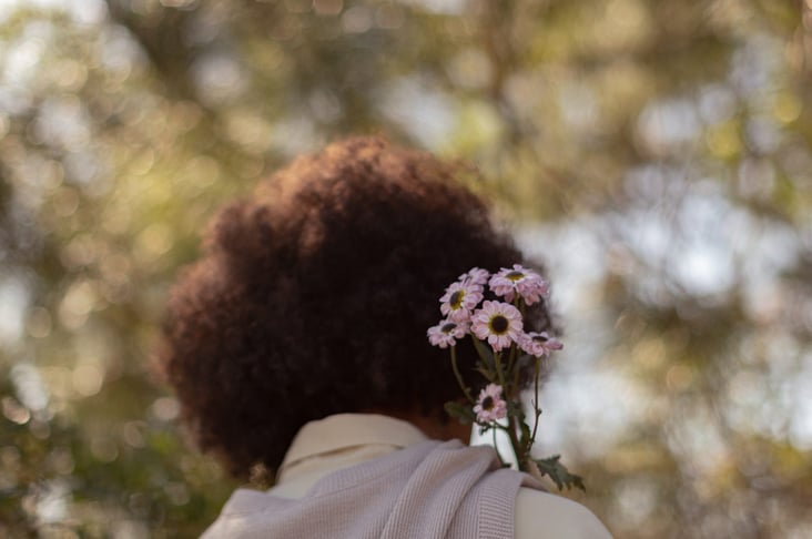 Woman with curly hair smiling and holding a bunch of purple flowers